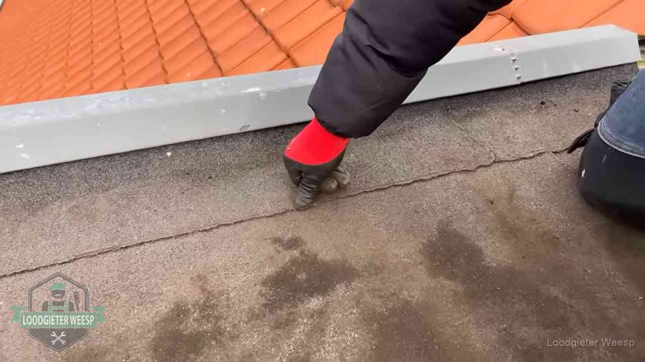 Vakman wijst een naad met vochtplekken aan op een bitumen plat dak in Weesp