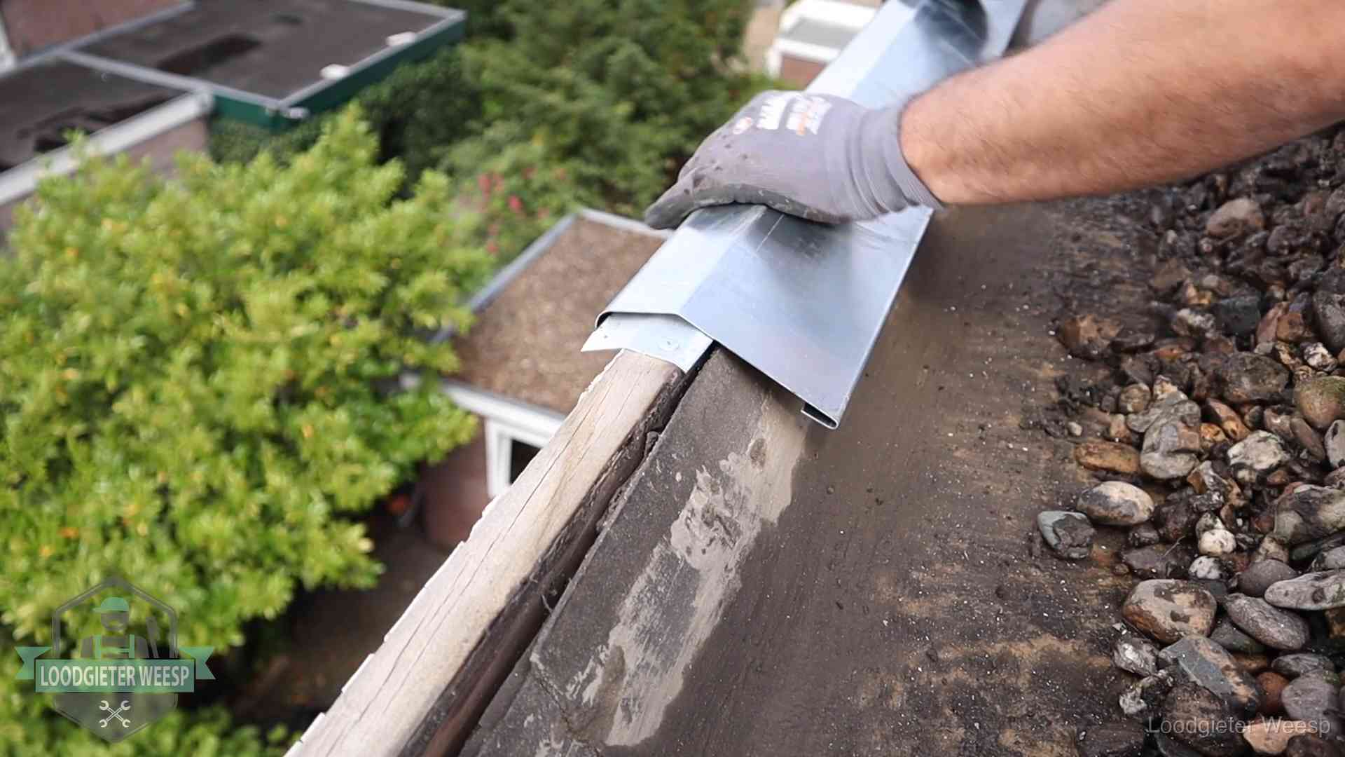 Dakdekker plaatst een zinken deklijst op een dakrand met uitzicht over een woonwijk in Weesp