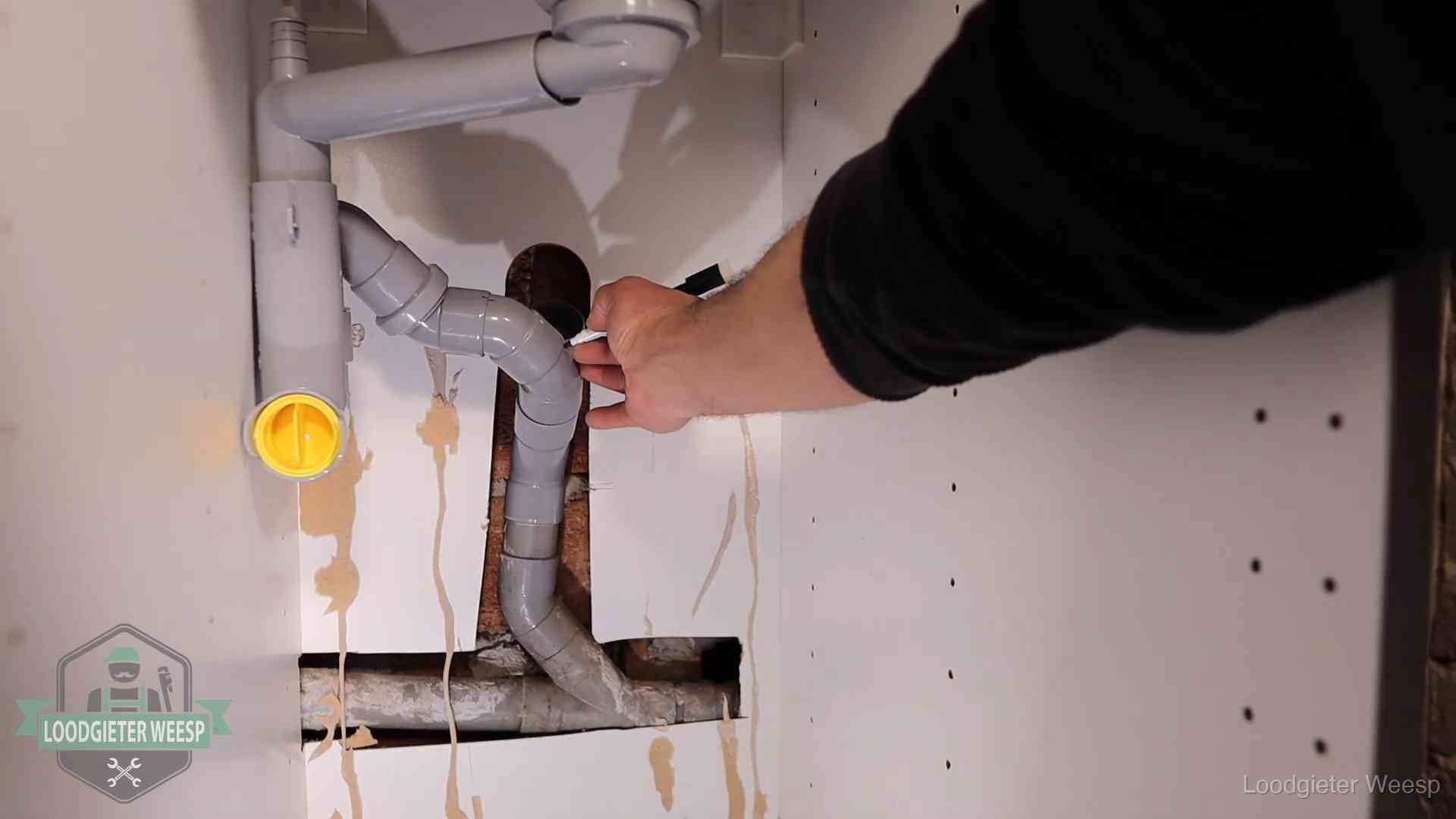 Loodgieter voor verhuurders en bedrijven in Weesp Loodgieter markeert een pvc-afvoerbuis onder een gootsteen in Weesp