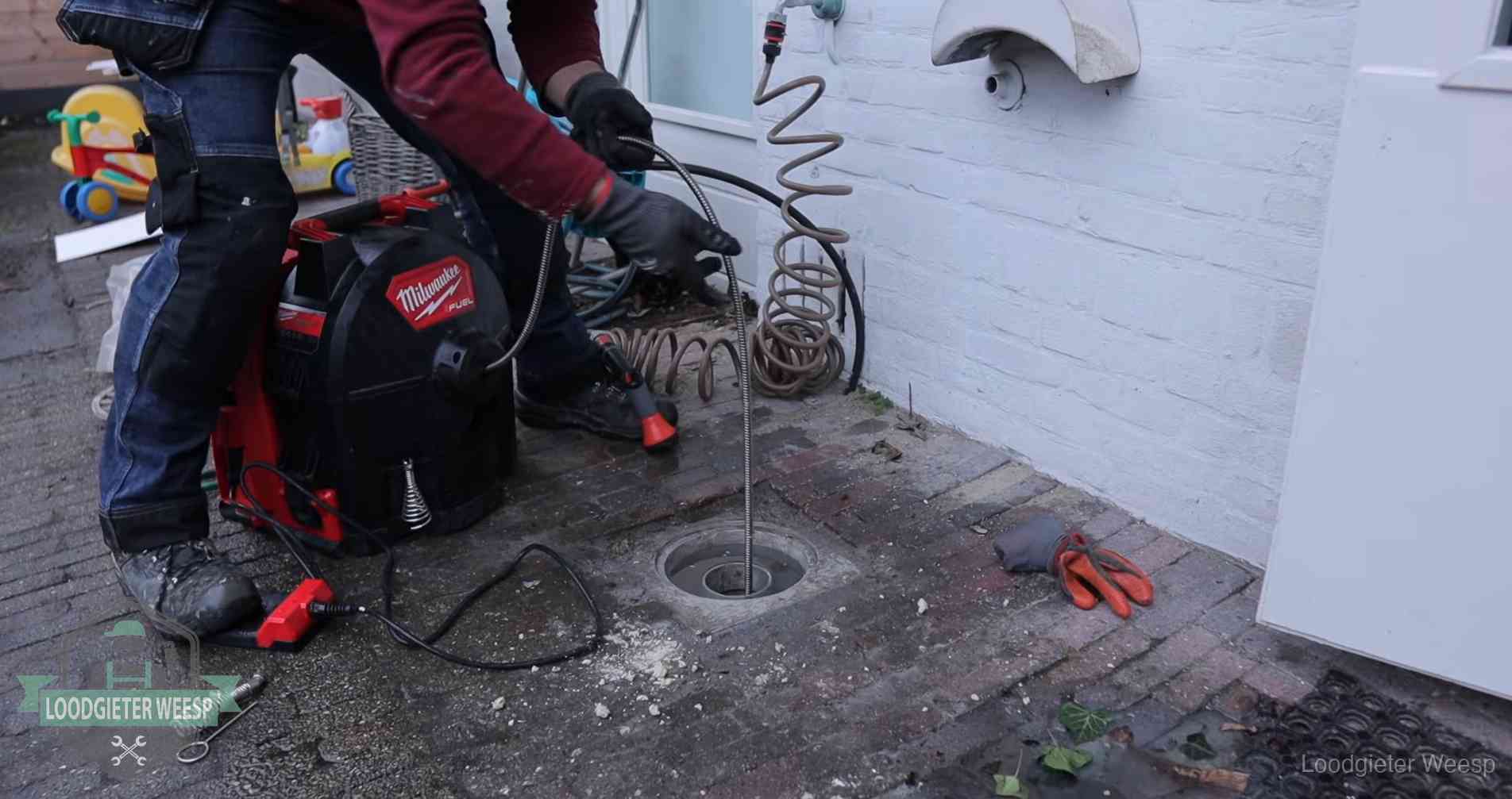 Ontstoppingsputje in de bestrating naast de gevel van een woning in Weesp