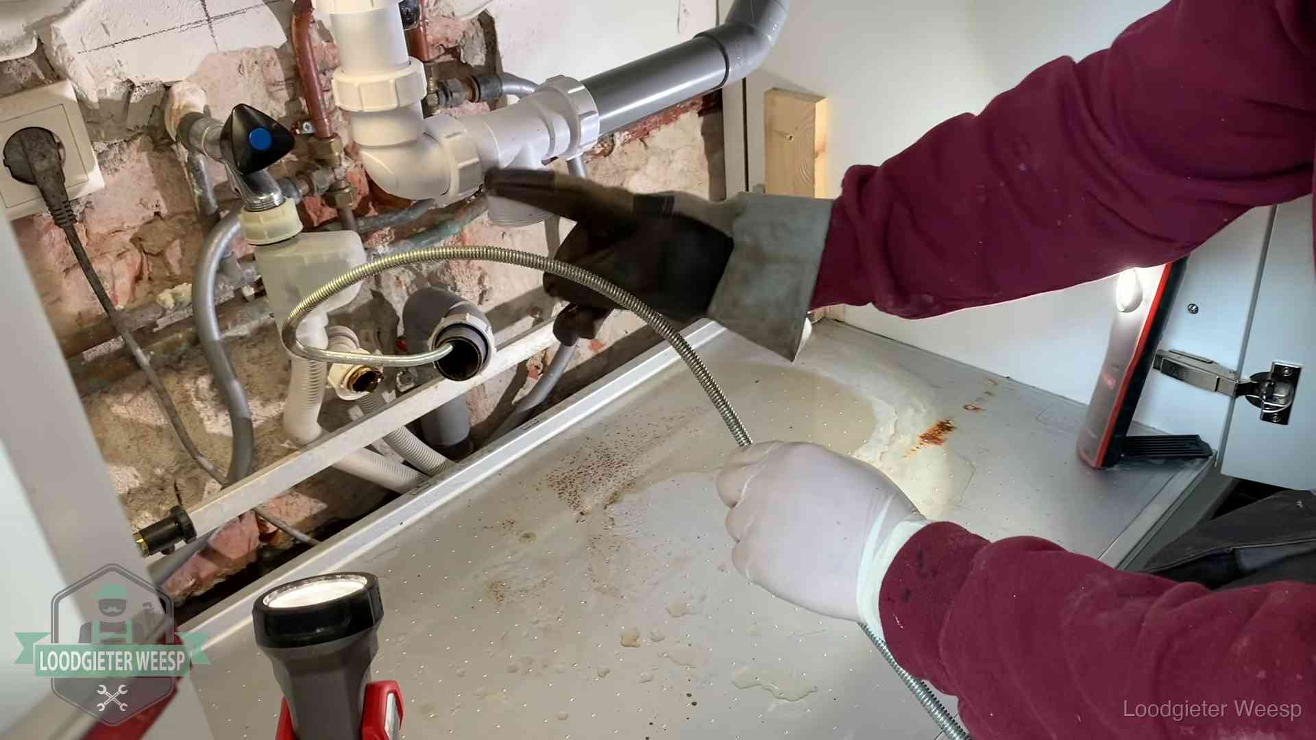 Ontstoppingsveer gaat in een geopende sifonaansluiting onder het aanrecht in Weesp