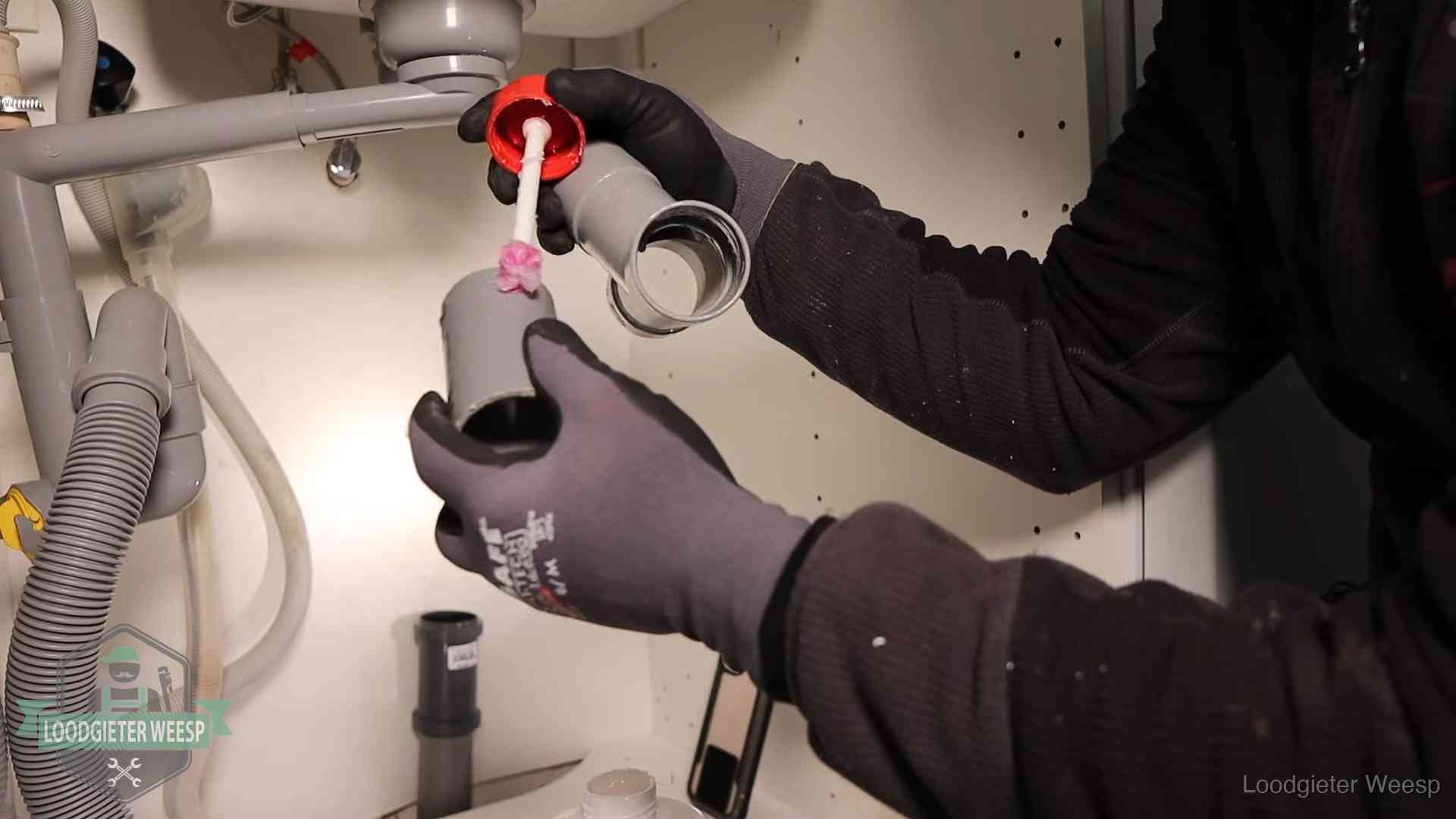 Loodgieter demonteert en reinigt de sifon onder een keukenkast in Weesp
