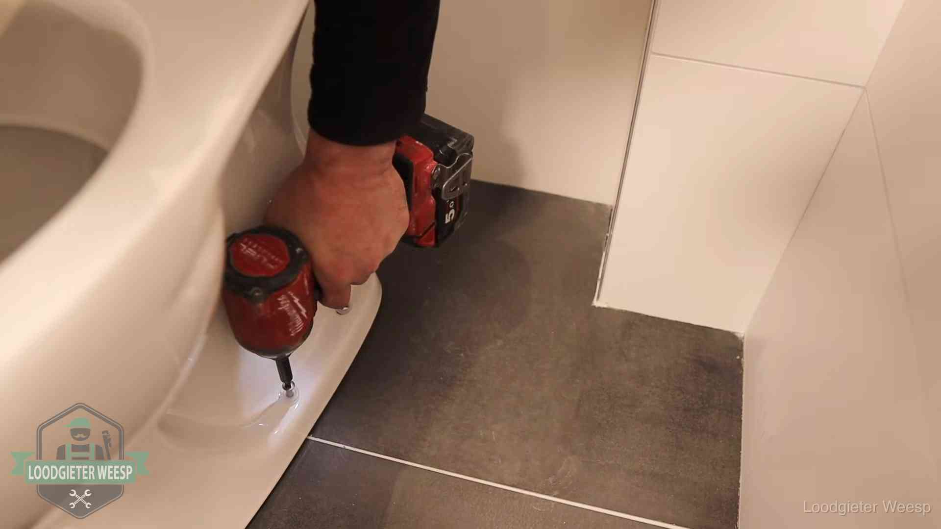 Kosten wc ontstoppen in Weesp Loodgieter zet de voet van een wc-pot vast op de tegelvloer in Weesp